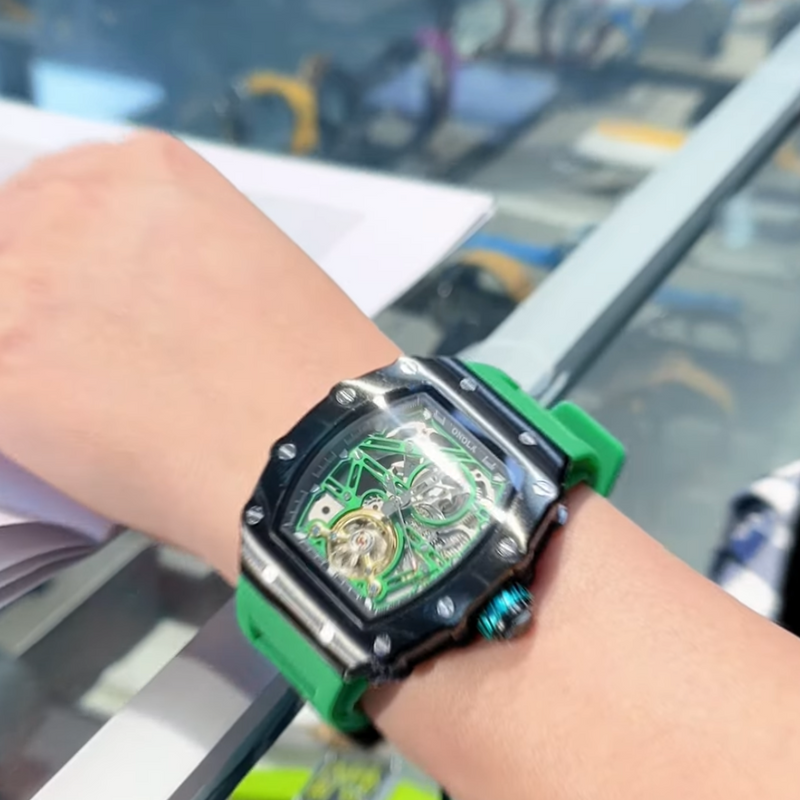 Close-up of a wrist wearing a green and black watch with a blurred indoor background